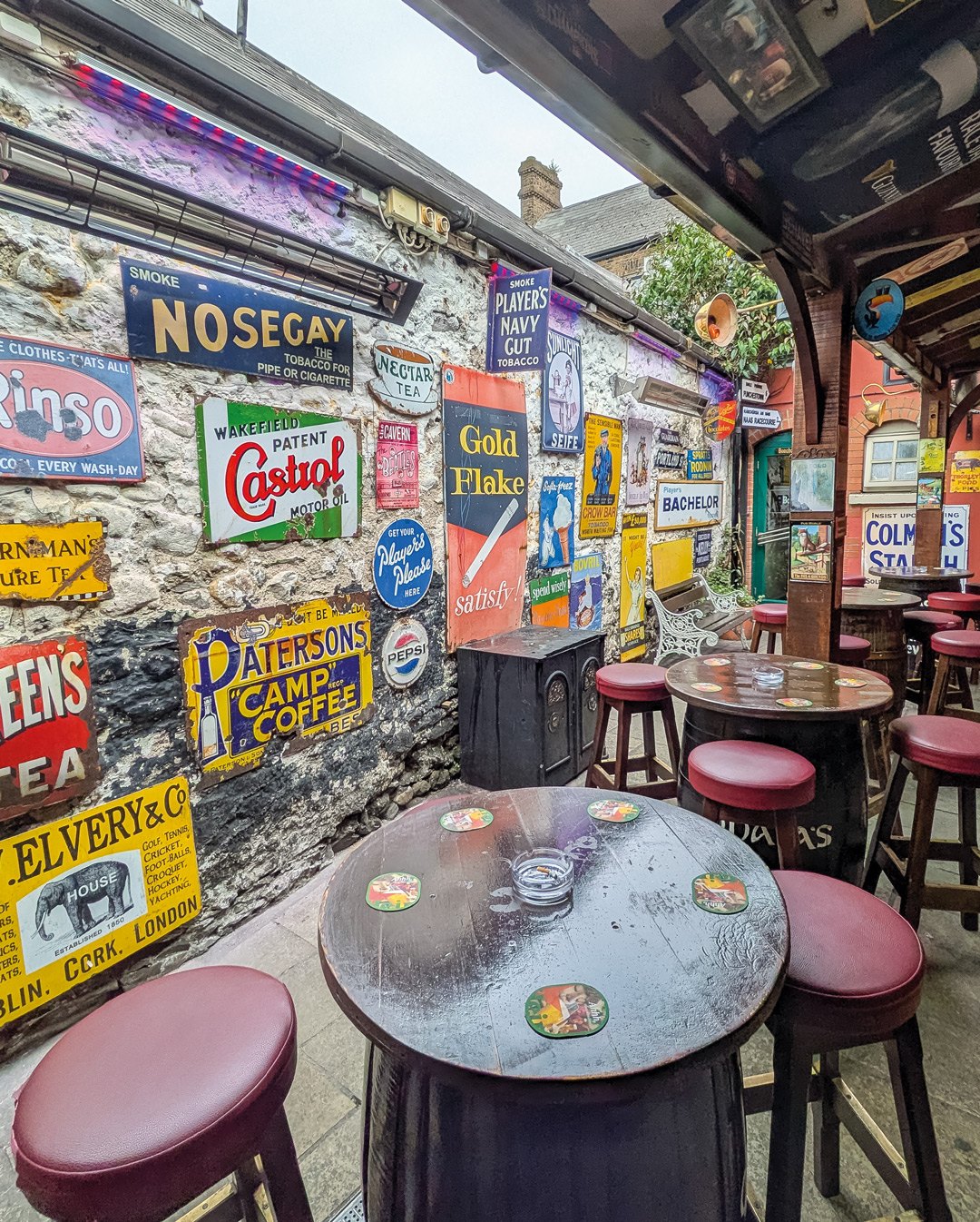 Tables and stools in the covered outdoor lounge, beside a wall of vintage advertising signs