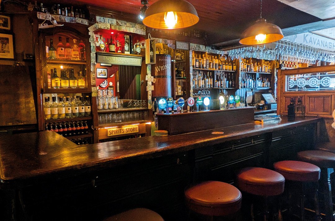 Warm wooden counter, bar stools and shelves of bottles in the Front Bar